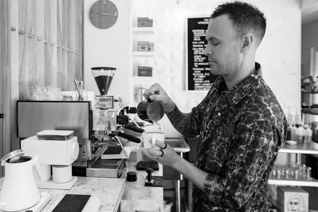Matt Lopez, owner of FVC Gallery coffee shop, standing behind the counter with art pieces displayed on the walls, creating a cozy and artistic atmosphere